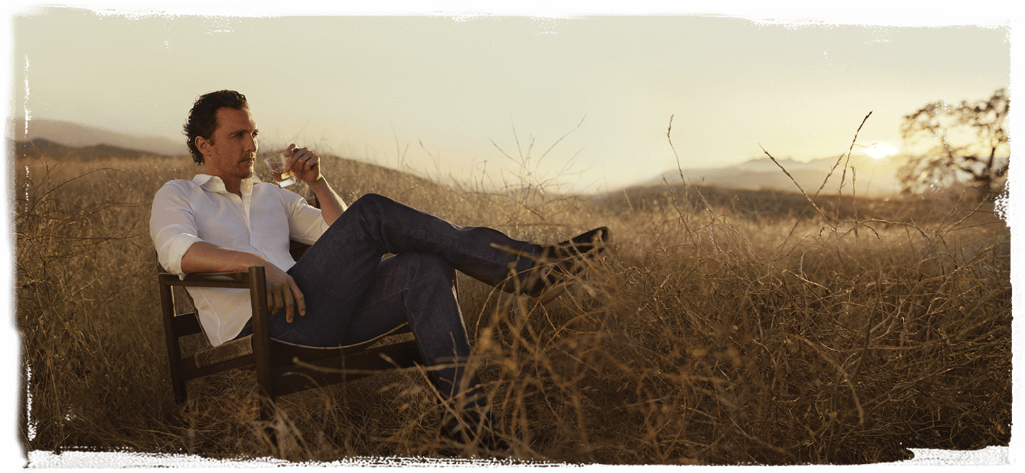 Matthew McConaughey siedzący w fotelu pośród zbóż ze szklaneczką Wild Turkey Longbranch